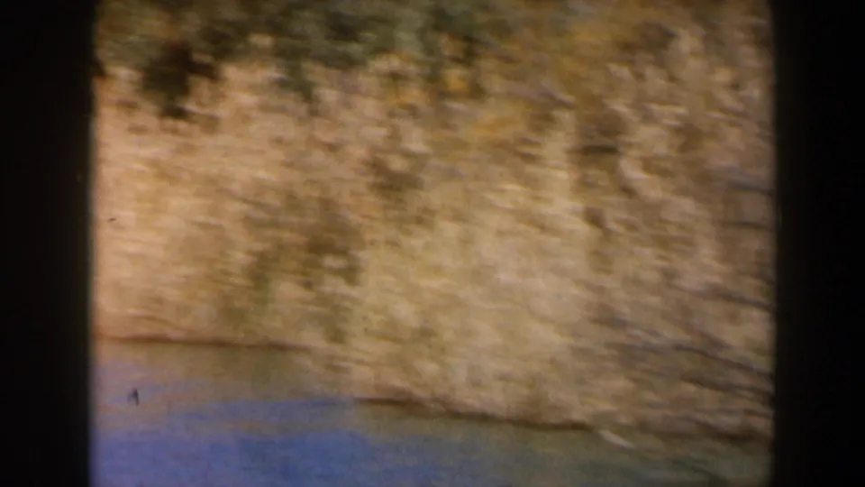 1960 8mm Israel footage showing water at the base of a rough, sunlit earth or stone bank, softened by motion blur.