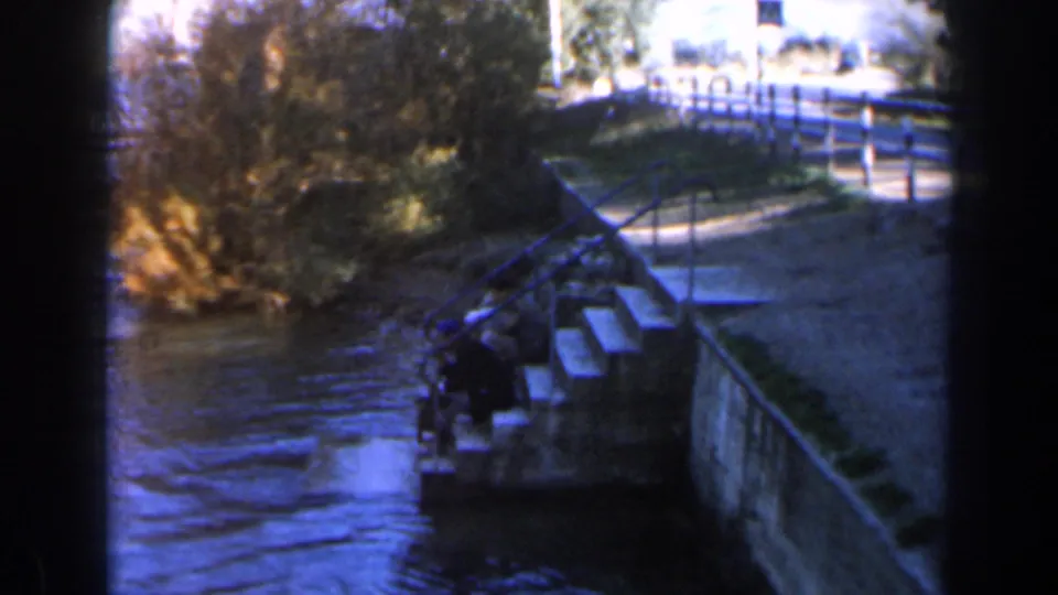 1960 Israel 8mm frame showing stone steps, metal railings, water, reeds, and a small indistinct person near the lower landing.