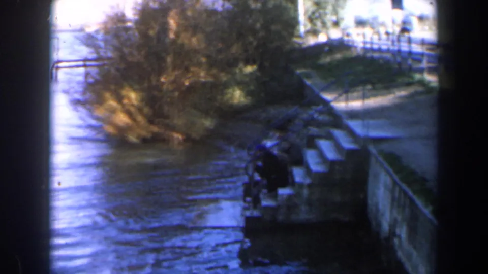 1960 Israel roadside water access with a stone stairway, railings, reeds, trees, and a small indistinct figure near the steps.