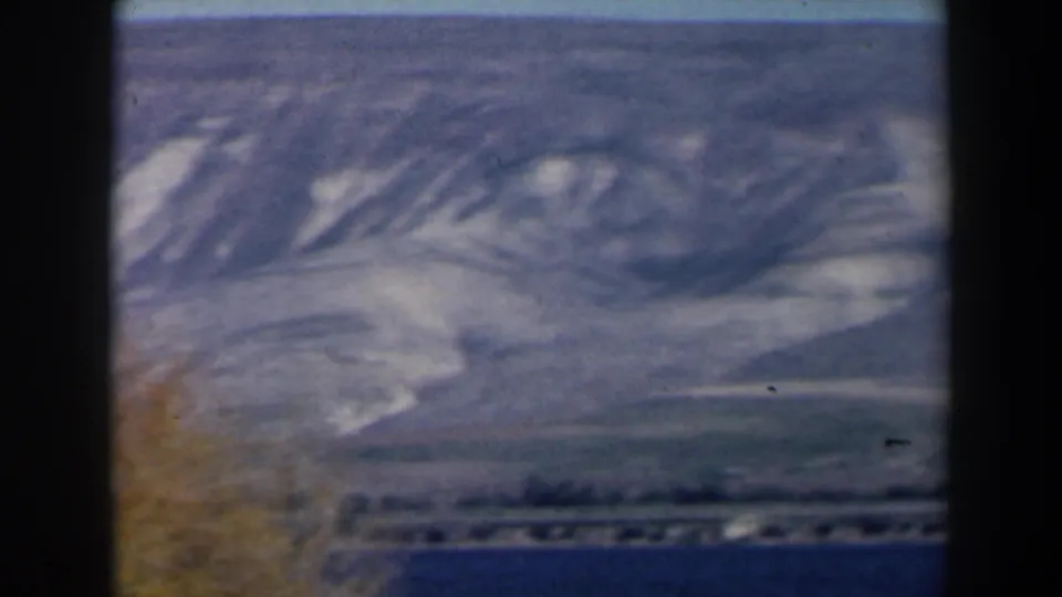 1960 8mm Israel view across lake water to a distant shore and pale arid mountain slopes.