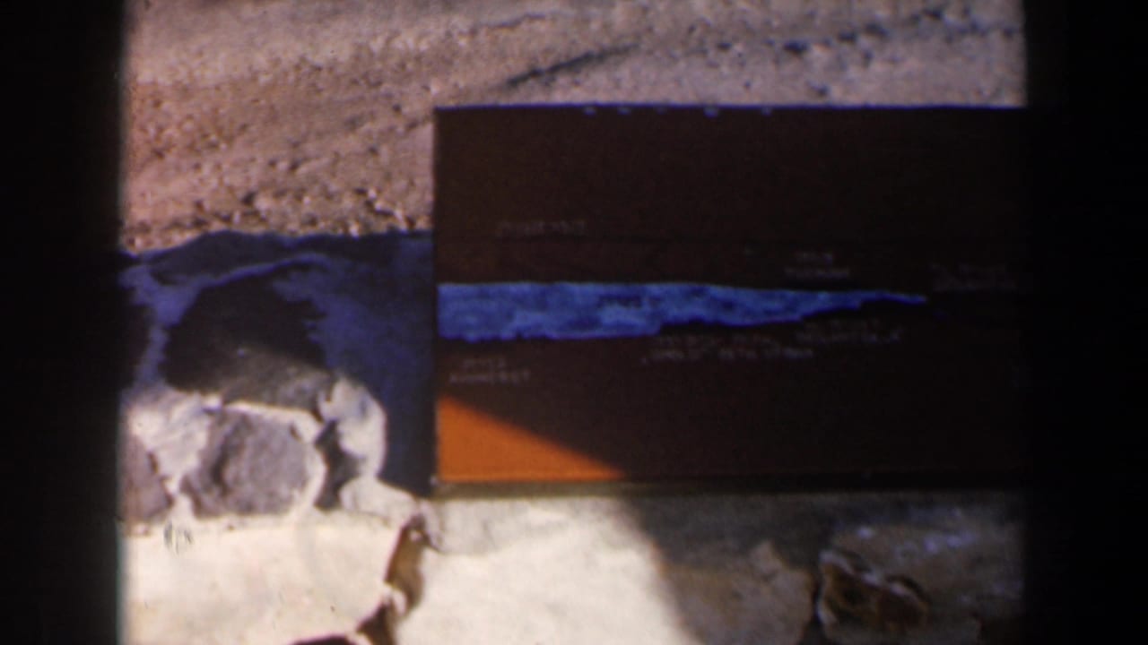 1960 Israel 8mm frame showing a brown tackle box with a blue stripe on grey rocks, partly obscured by dark frame edges.