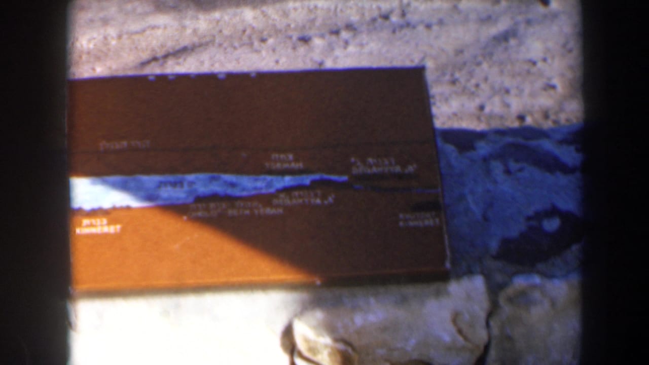 Close view of the brown plaque with place names, blue line, stones, and shadow.