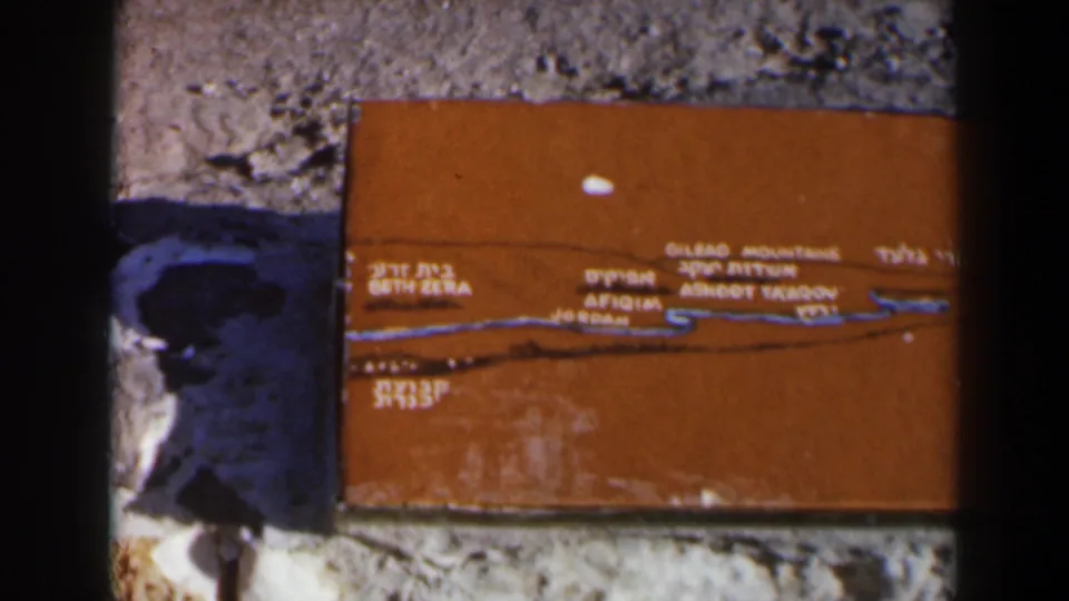 1960 Israel frame showing the brown informational plaque with bilingual text, a blue route line, stones, and gravel.