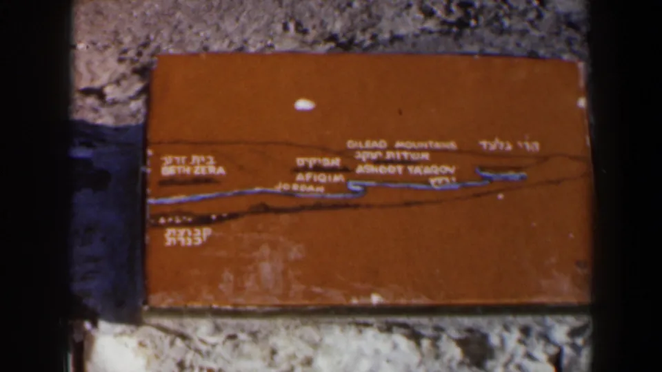 Close 8mm view of an orange Israel location plaque with Hebrew and English text and a blue route or boundary line.