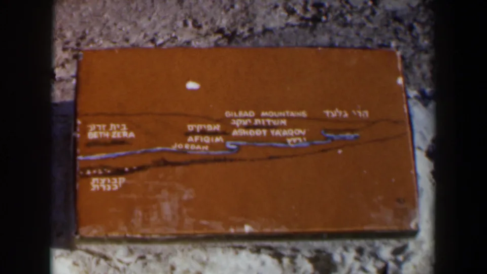 1960 Israel home-movie frame of a weathered orange geographic plaque with legible regional place labels.