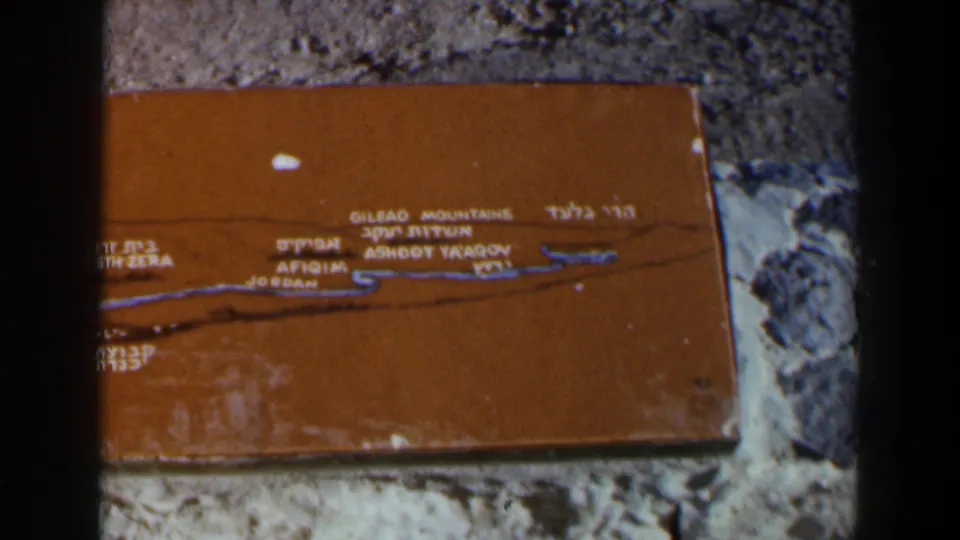 Final 8mm frame showing the orange Hebrew and English map plaque against rough stone in Israel.