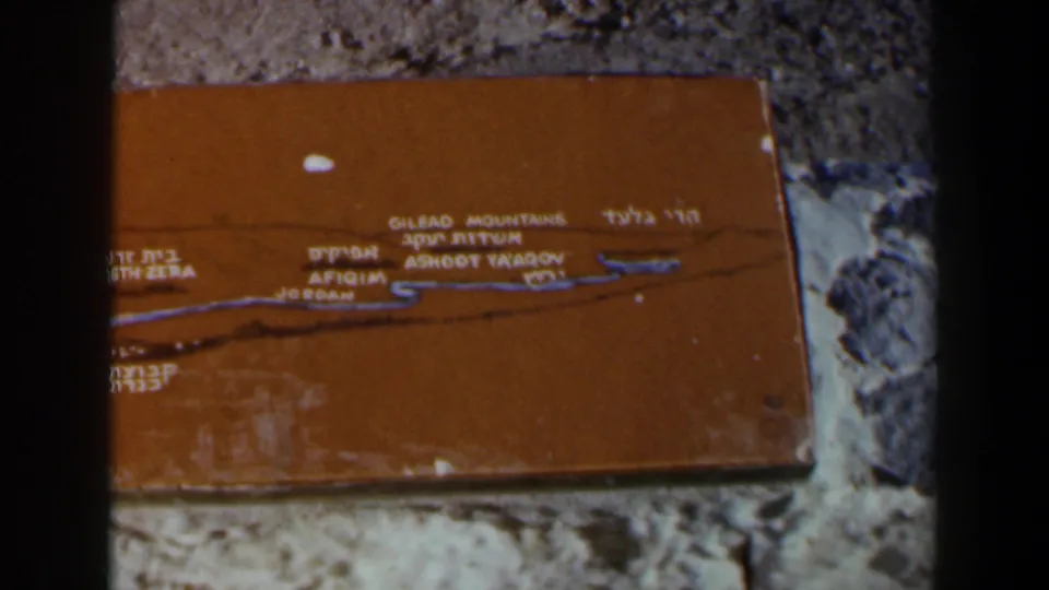 Weathered bilingual plaque identifying regional locations, framed tightly with visible film gate shadow.