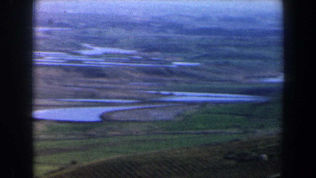 Aerial farmland with reflective ponds and layered field patterns in the distance.