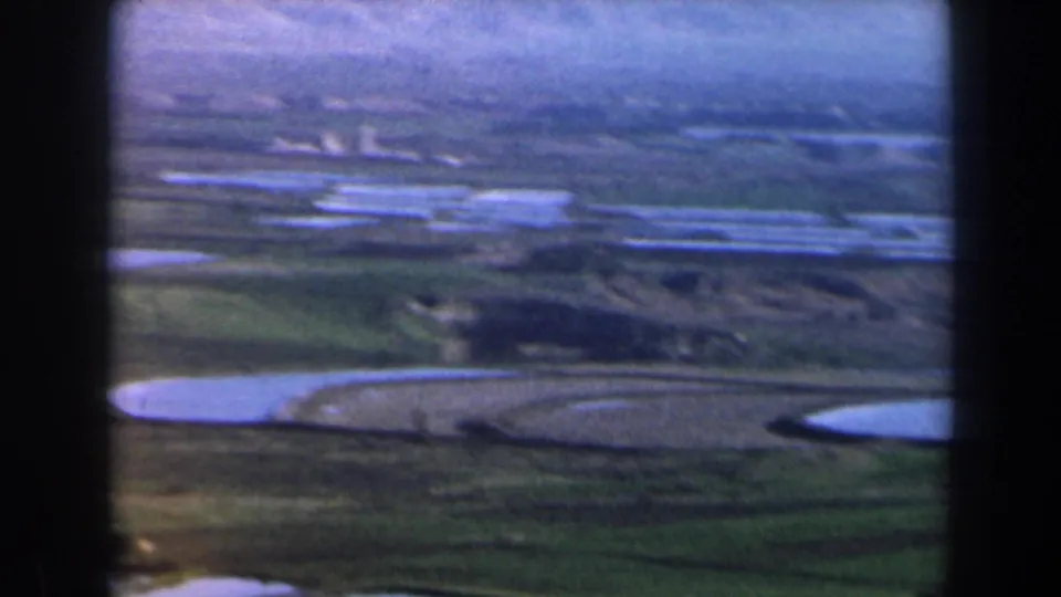 1960 Israel 8mm aerial frame showing rural fields, pale water surfaces, and soft blue-purple film tones.