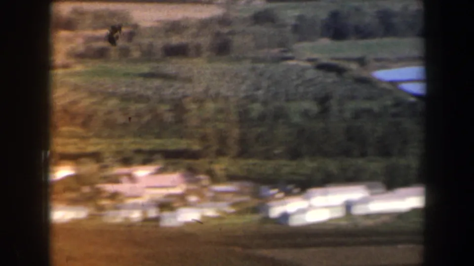 1960 Israel home-movie view of a lower hillside, with fields, scattered trees, pale buildings, and water visible near the foreground.