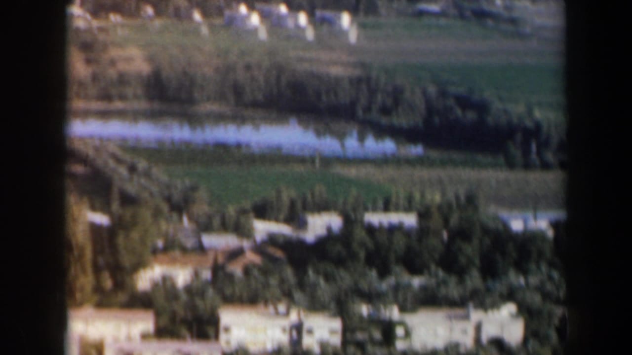 Distant town buildings, trees, fields, and narrow lakes seen through dark film borders.