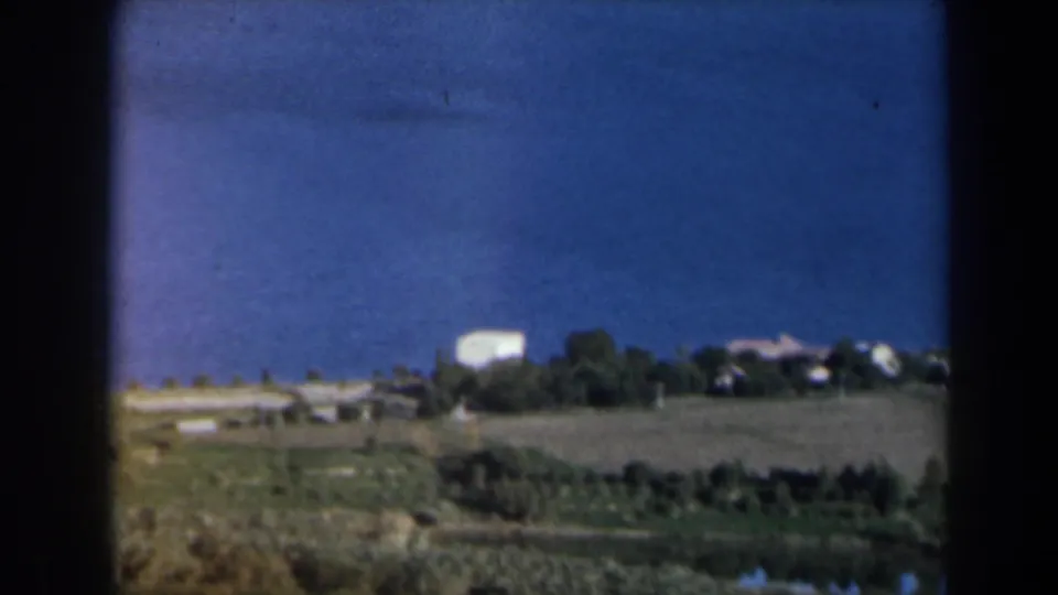 1960 Israel home-movie view of open farmland with dark tree lines and pale buildings on the horizon.