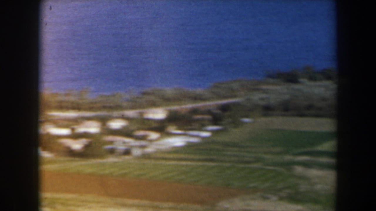 Green hillside with pale clustered buildings and open fields.