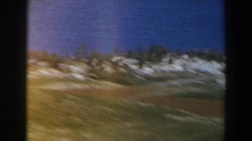 Soft 8mm view of cultivated fields and a ridge of pale buildings in 1960 Israel.