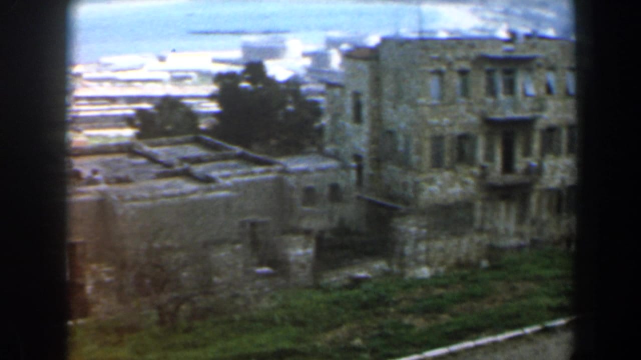 Weathered stone buildings on a green hillside with coastline in the distance.