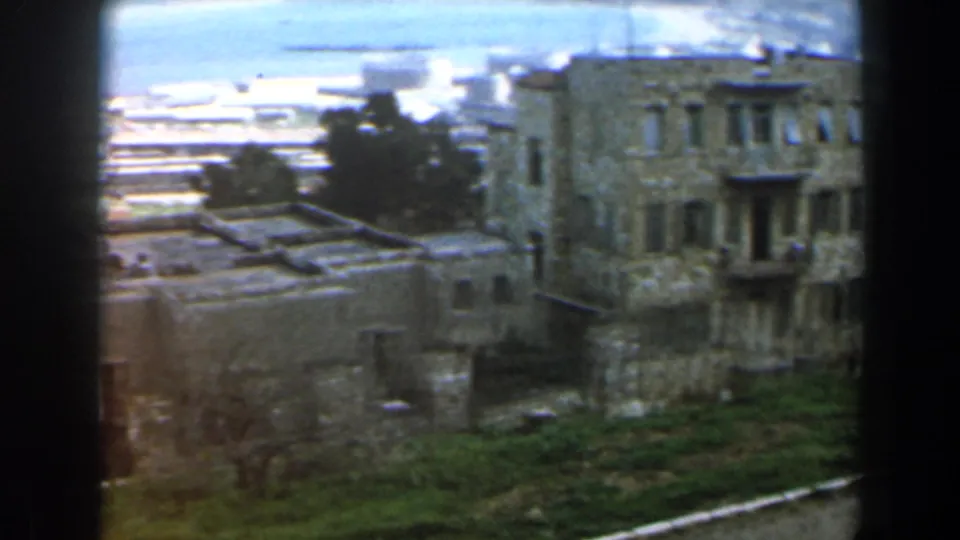 1960 Israel 8mm view of clustered stone buildings on a hillside overlooking a distant coast or waterfront area.