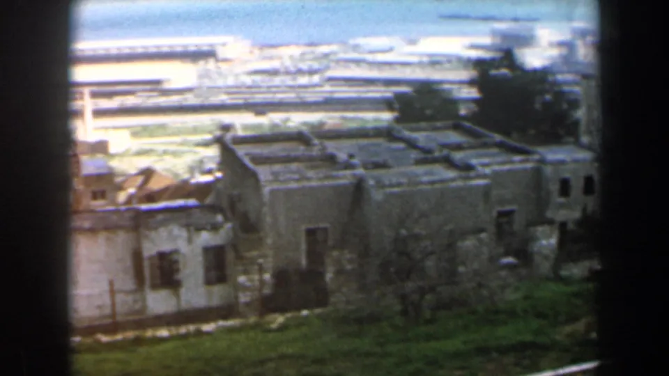 Elevated 1960 Israel home-movie frame showing dense low buildings and a larger weathered structure near a distant waterfront.