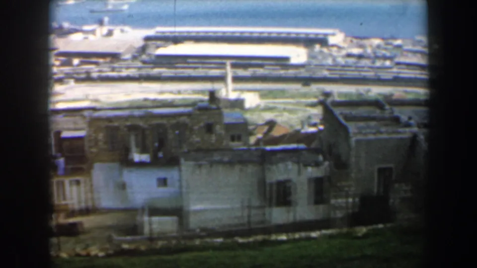 1960 Israel 8mm frame of flat-roofed urban houses below a distant waterfront or port-like area.