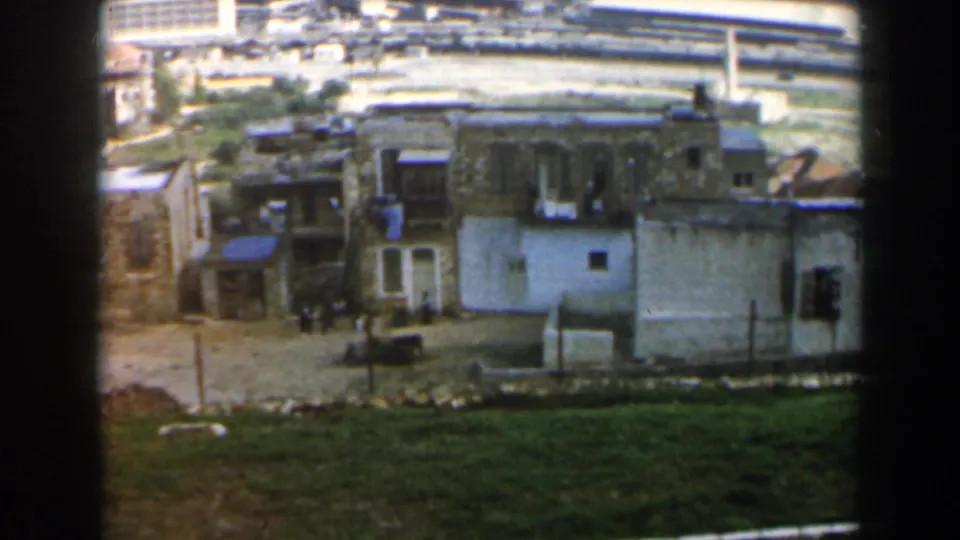 1960 Israel home-movie view of modest hillside buildings, open ground, and a distant coast or port area.
