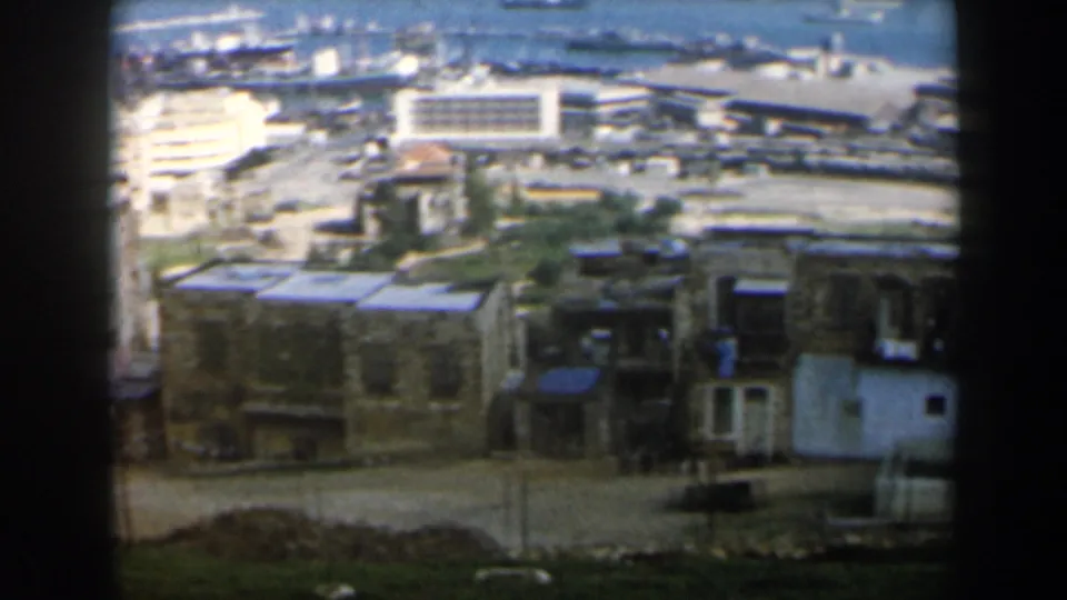 1960 Israel coastal view with tan buildings in the foreground and harbor infrastructure near the sea.
