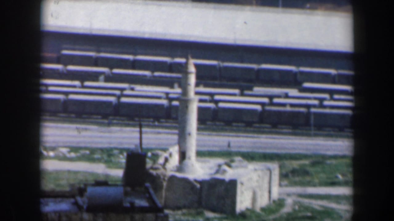 Freight cars and rail tracks beside a small white tower near industrial buildings.
