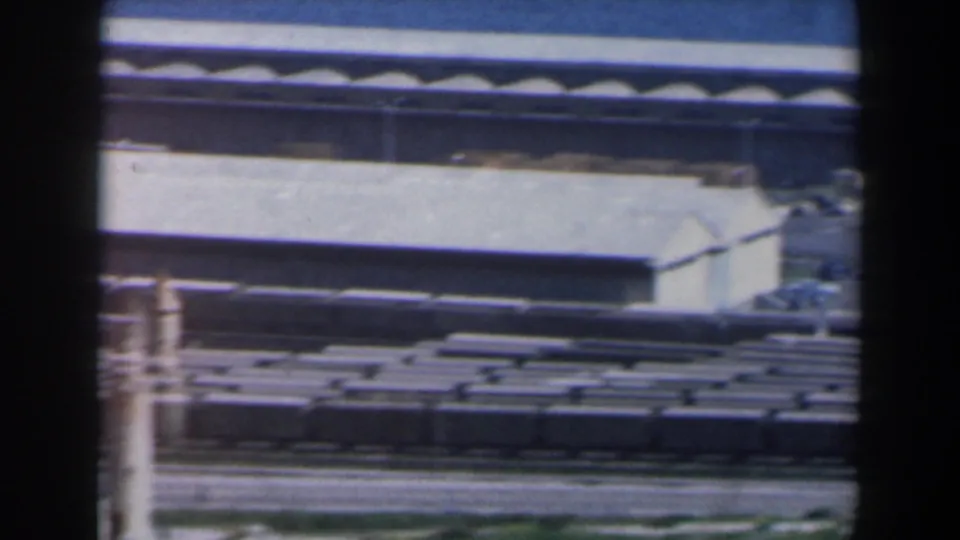 1960 Israel port-area frame with rail freight cars, tracks, low warehouse buildings, and a partial foreground structure.