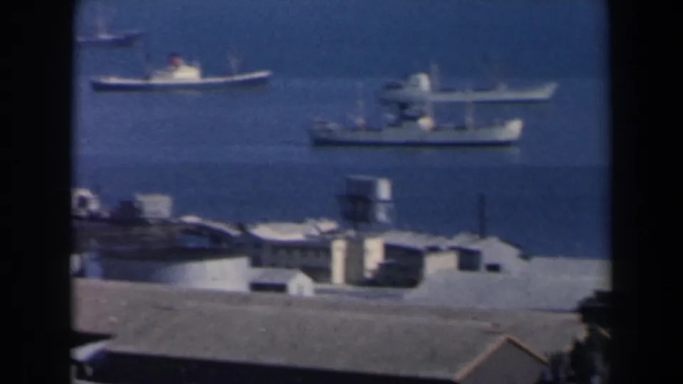 1960 Israel harbor view with ships on blue water and low waterfront structures in the foreground.