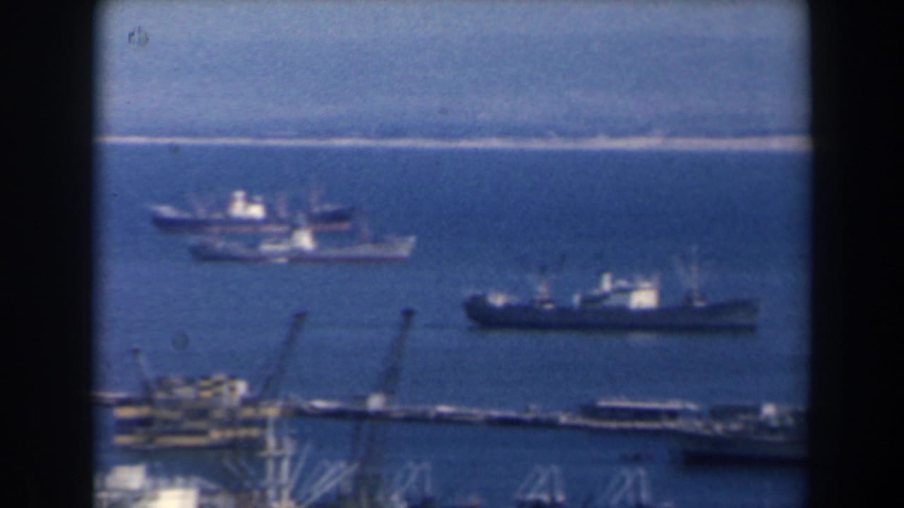 Ships and harbor structures seen across a blue coastal port.