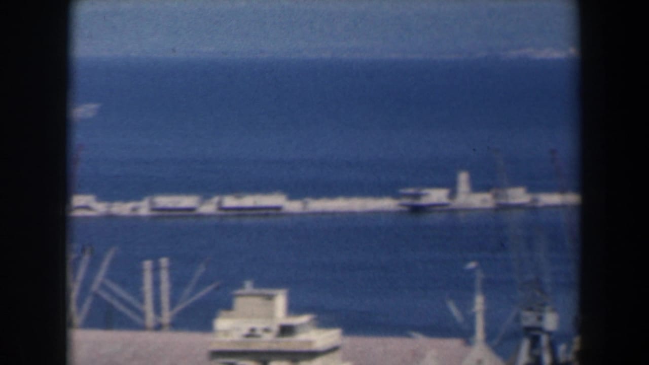 Harbor waterfront with piers, small vessel, breakwater, and open blue water.