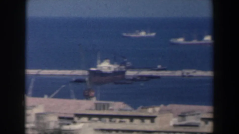 Elevated 1960 Israel harbor frame showing a large vessel by the pier, smaller boats, and distant ships on blue water.