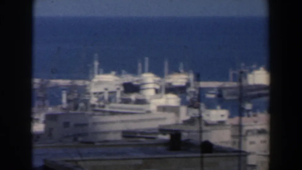Soft 8mm frame of an Israeli port area in 1960 with docked boats, waterfront buildings, and industrial harbor structures.