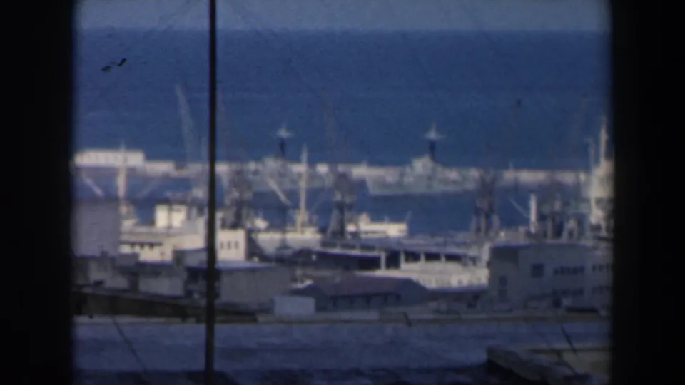 1960 Israel port view with cranes, moored boats, piers, and the blue sea beyond, framed by 8mm film edges.