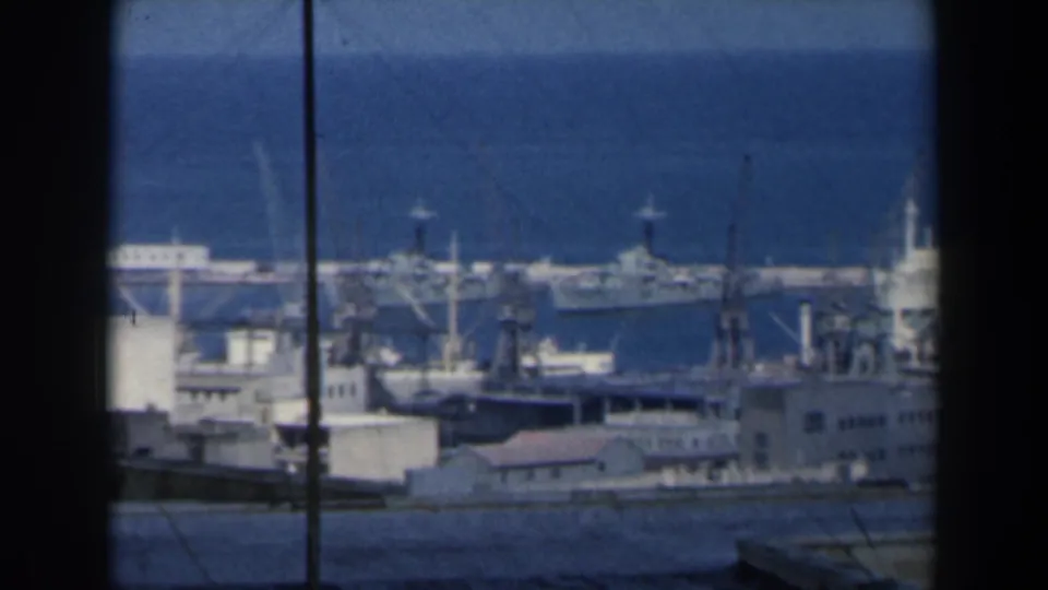 1960 Israel harbor footage frame showing ships and cranes along the waterfront with poles and wires crossing the distant sea view.