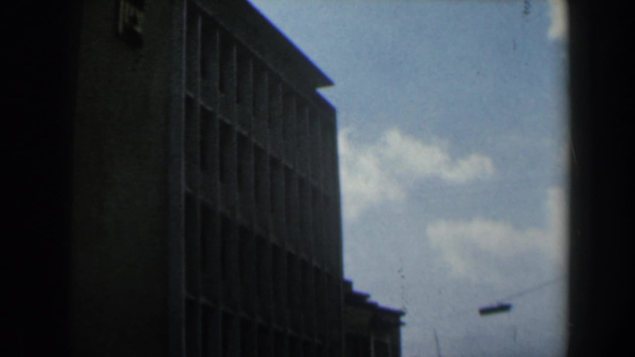 1960 Israel 8mm frame showing a tall brick or concrete building with vertical window bays under a pale cloudy sky.