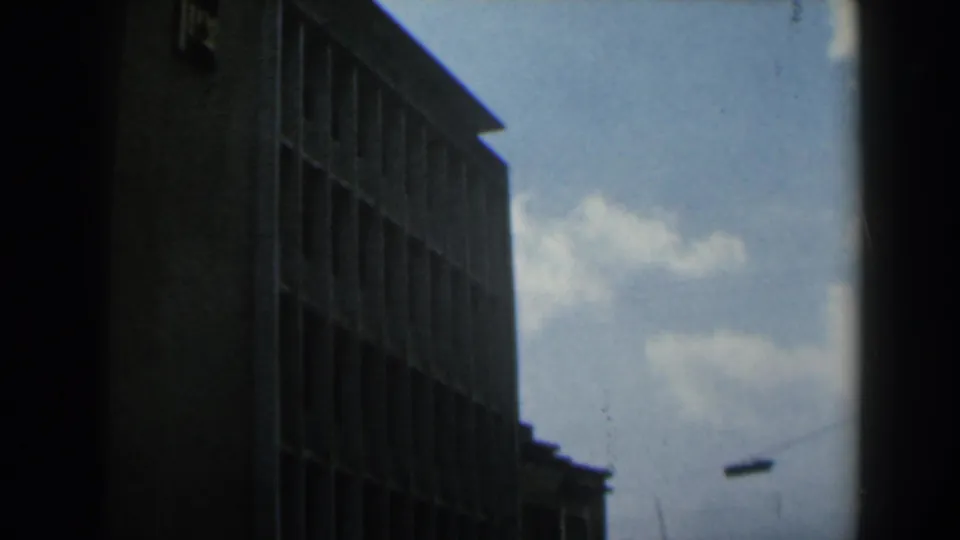 1960 Israel 8mm frame showing a tall brick or concrete building with vertical window bays under a pale cloudy sky.