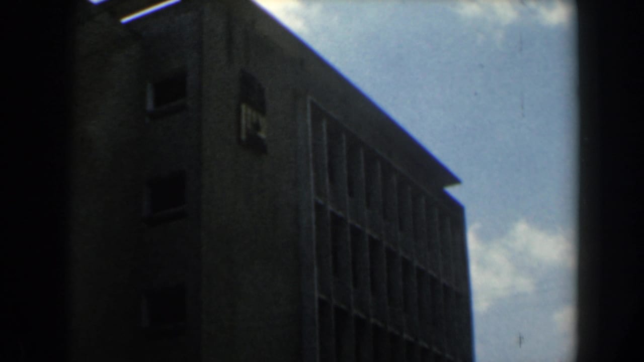 Dark building corner with rows of windows and sky visible through an obstructed frame.