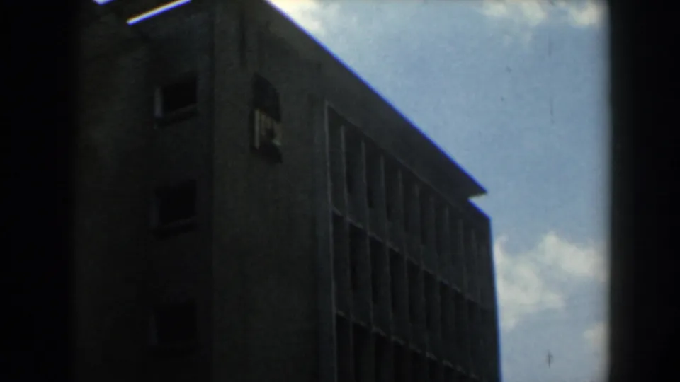 1960 Israel 8mm frame of a shadowed multi-story building corner with repeated windows and dark border obstruction.