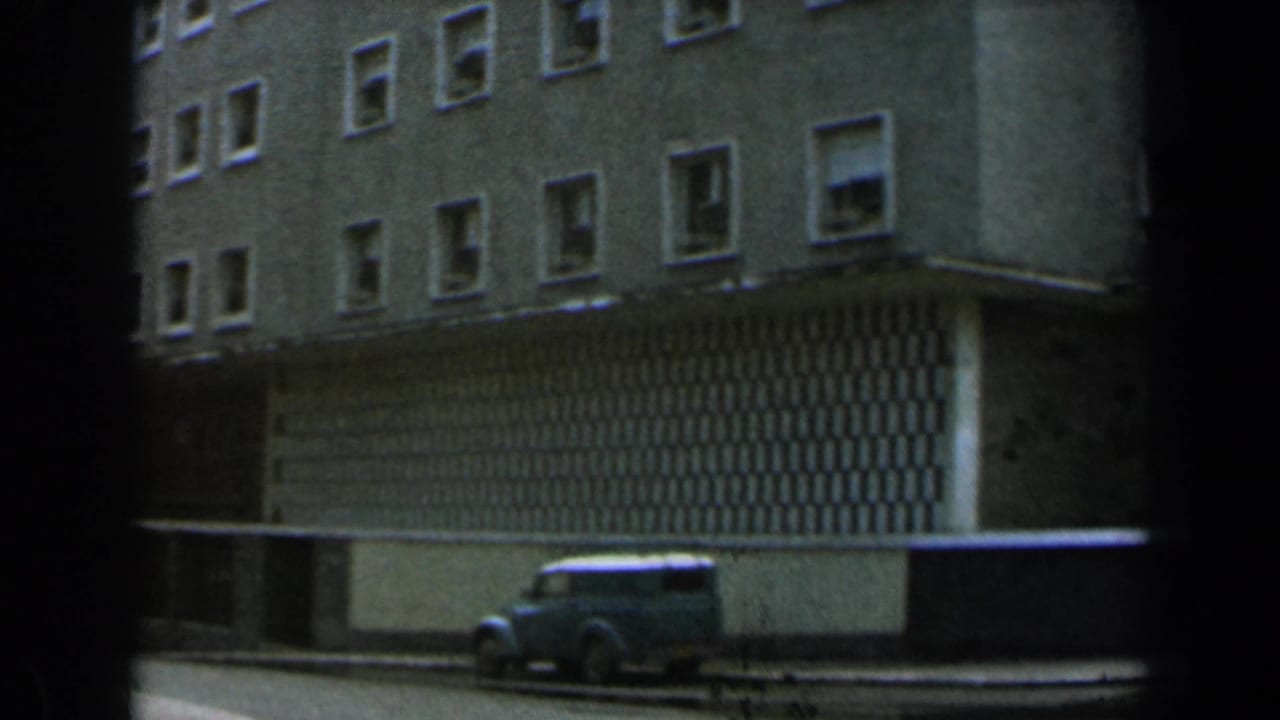 Parked light blue van beside a multi-story building with patterned facade panels.