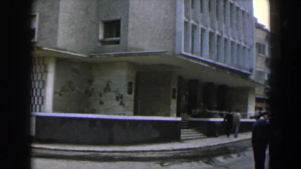1960 Israel street scene with a building entrance, steps, low wall, and adults moving along the sidewalk.