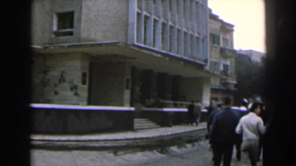 1960 Israel urban sidewalk view with well-dressed adults conversing near a low wall and weathered building entrance.