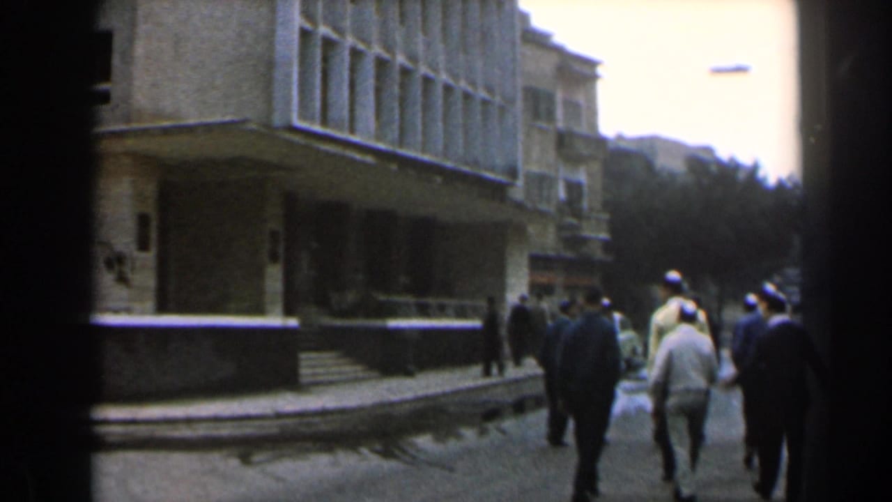 Several people walk away from the camera along the street beside the building.