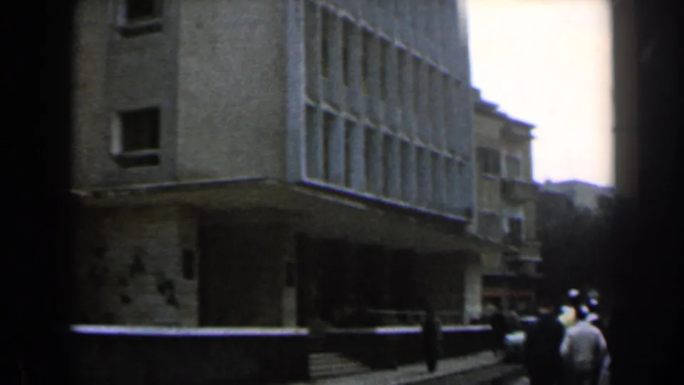 Soft 8mm view of a 1960 Israel sidewalk with walkers near steps and a light building exterior.
