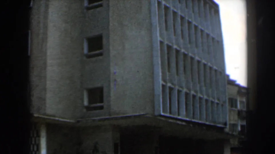 1960 Israel home-movie frame showing a light building corner, gridded windows, and pedestrians below.