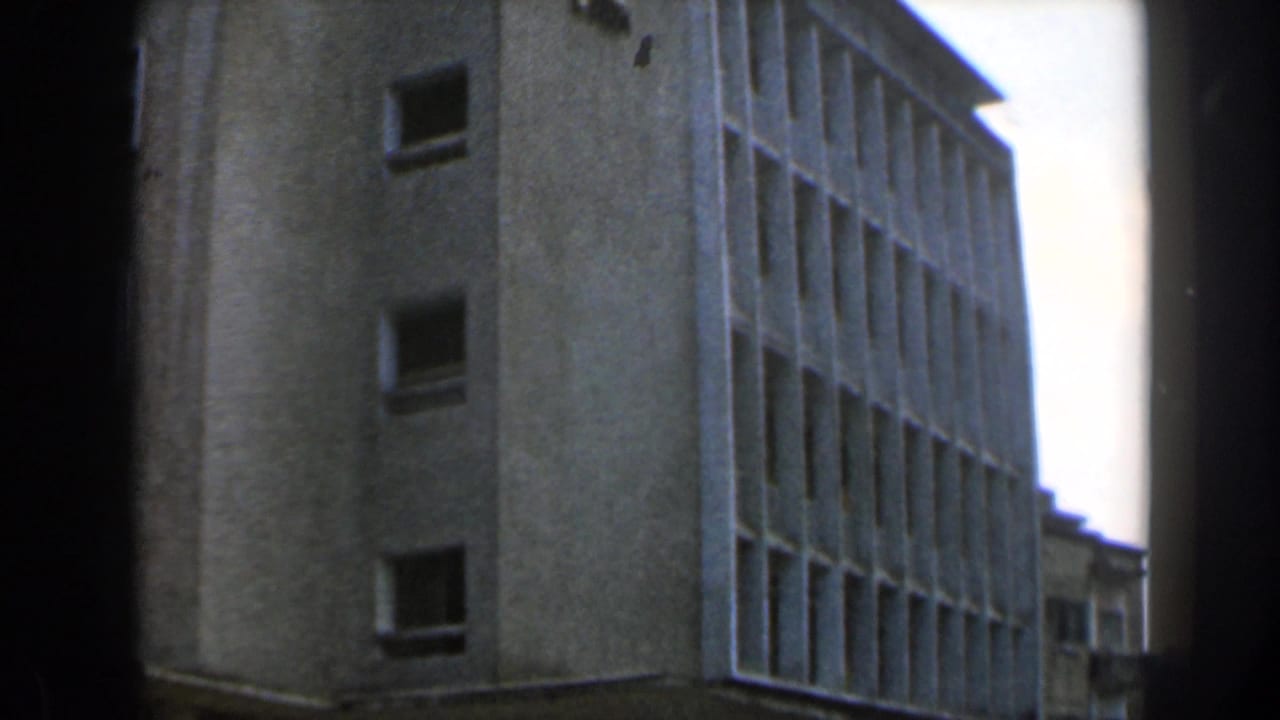 1960 Israel 8mm frame showing a stark concrete modernist building from below, with window grids, pale sky, and visible film-frame edges.