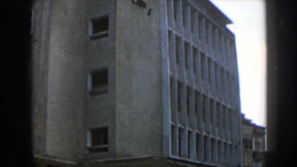 1960 Israel 8mm frame showing a stark concrete modernist building from below, with window grids, pale sky, and visible film-frame edges.
