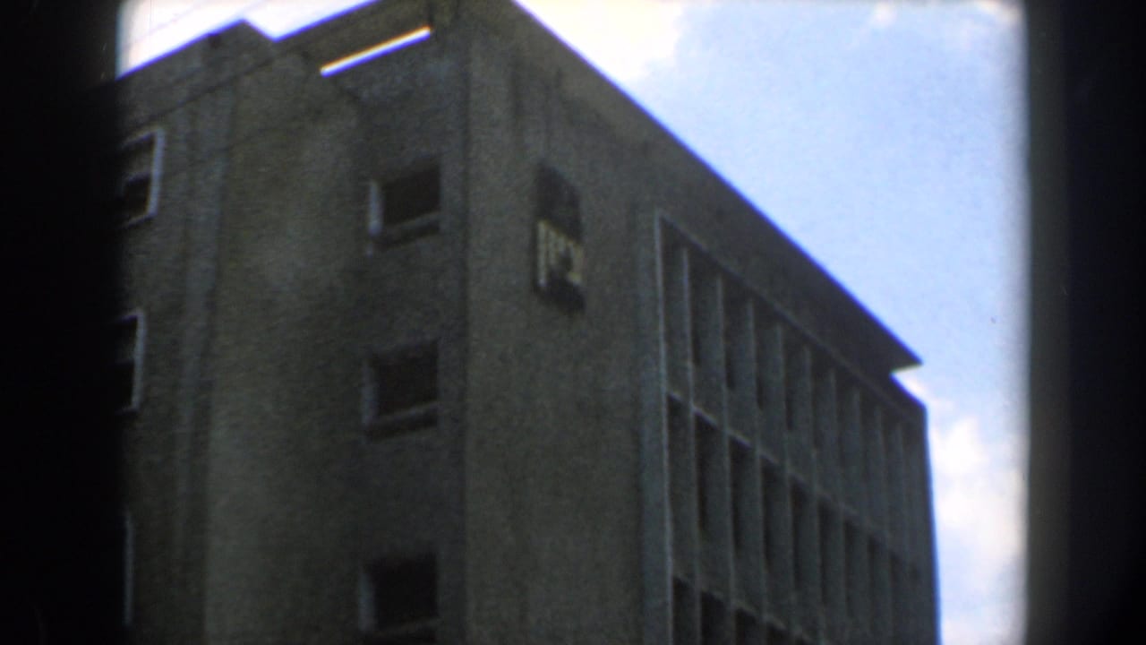 Concrete building corner seen from below, with small windows and a bright sky behind it.