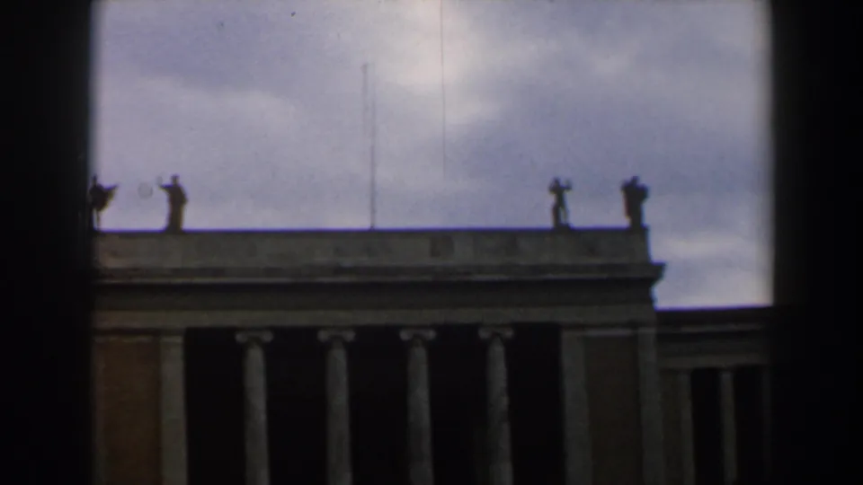 1960 Israel 8mm frame with rooftop statues, a cloudy sky, columns, and a dark edge partly blocking the building.