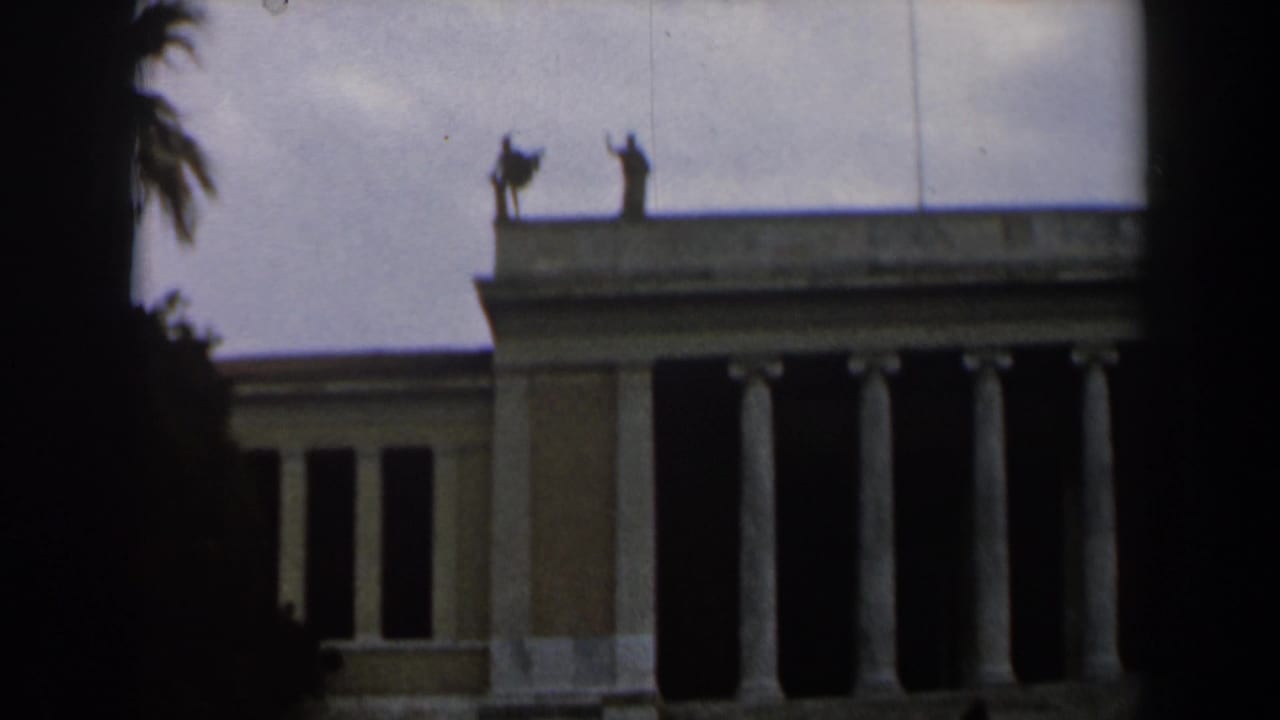 Columned civic building facade with roofline statues and dark film edges.