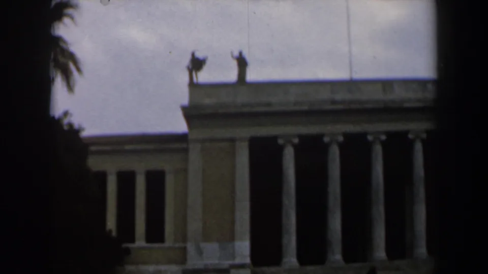 1960 Israel 8mm view of a large columned civic building facade, with roofline statues and heavy dark vignetting at the frame edges.