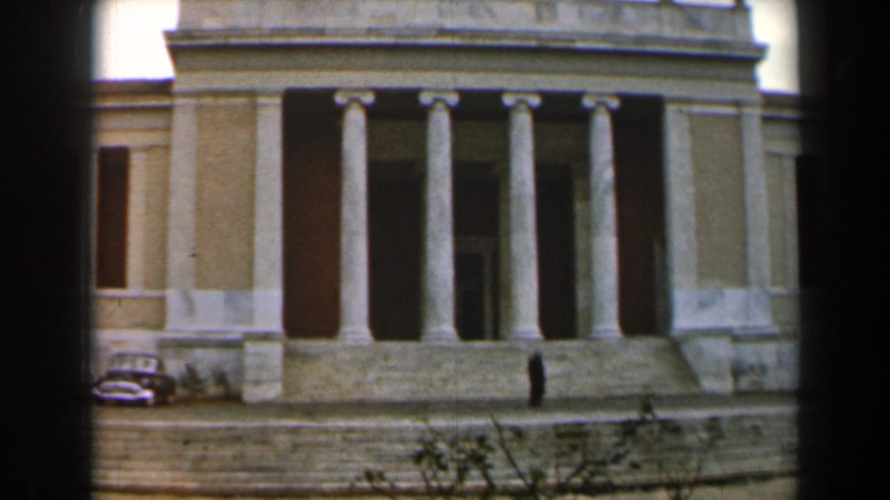 Large columned building with parked car and a person near the steps.